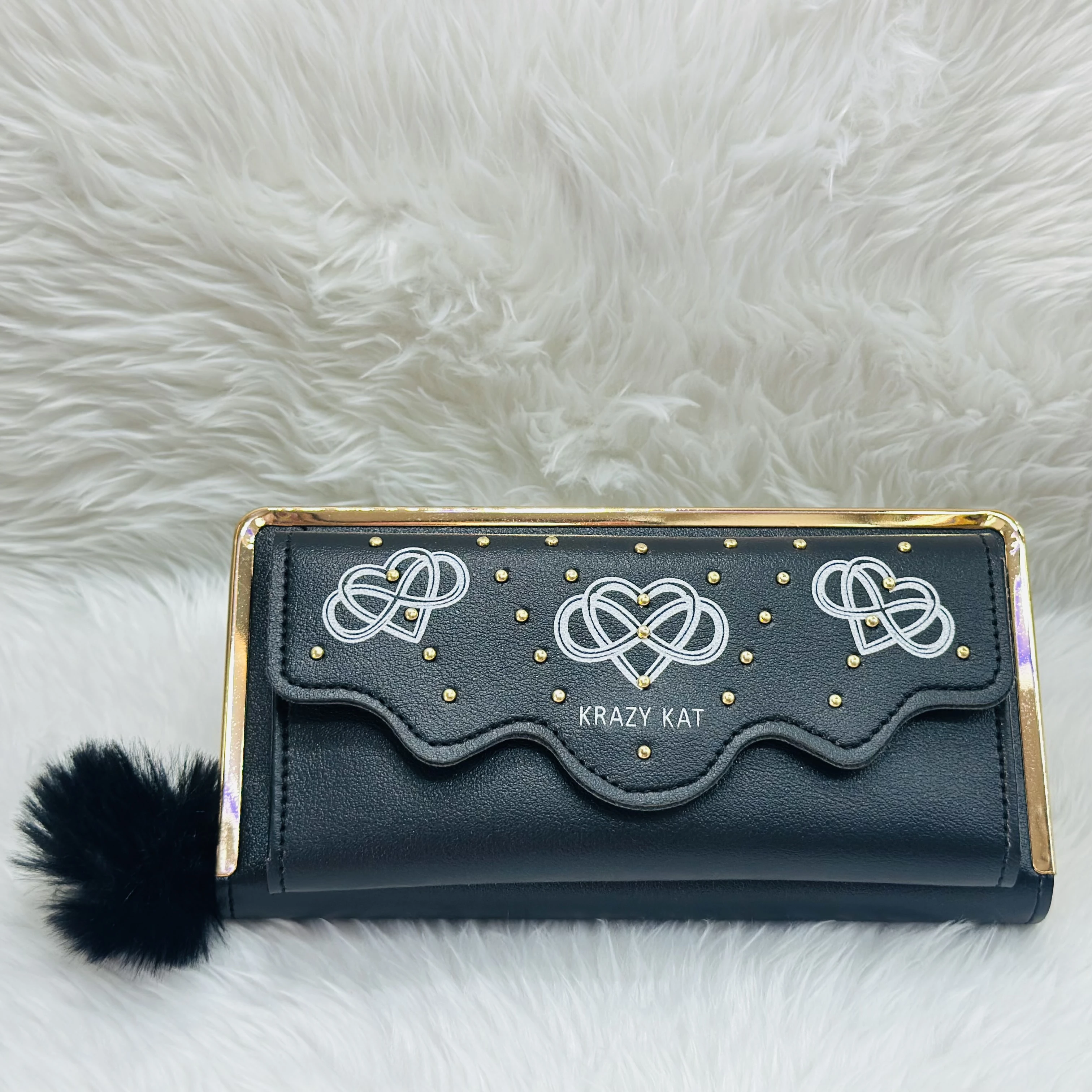 Black women's wallet with a gold frame and a flap decorated with white knot-style heart patterns and small gold studs.