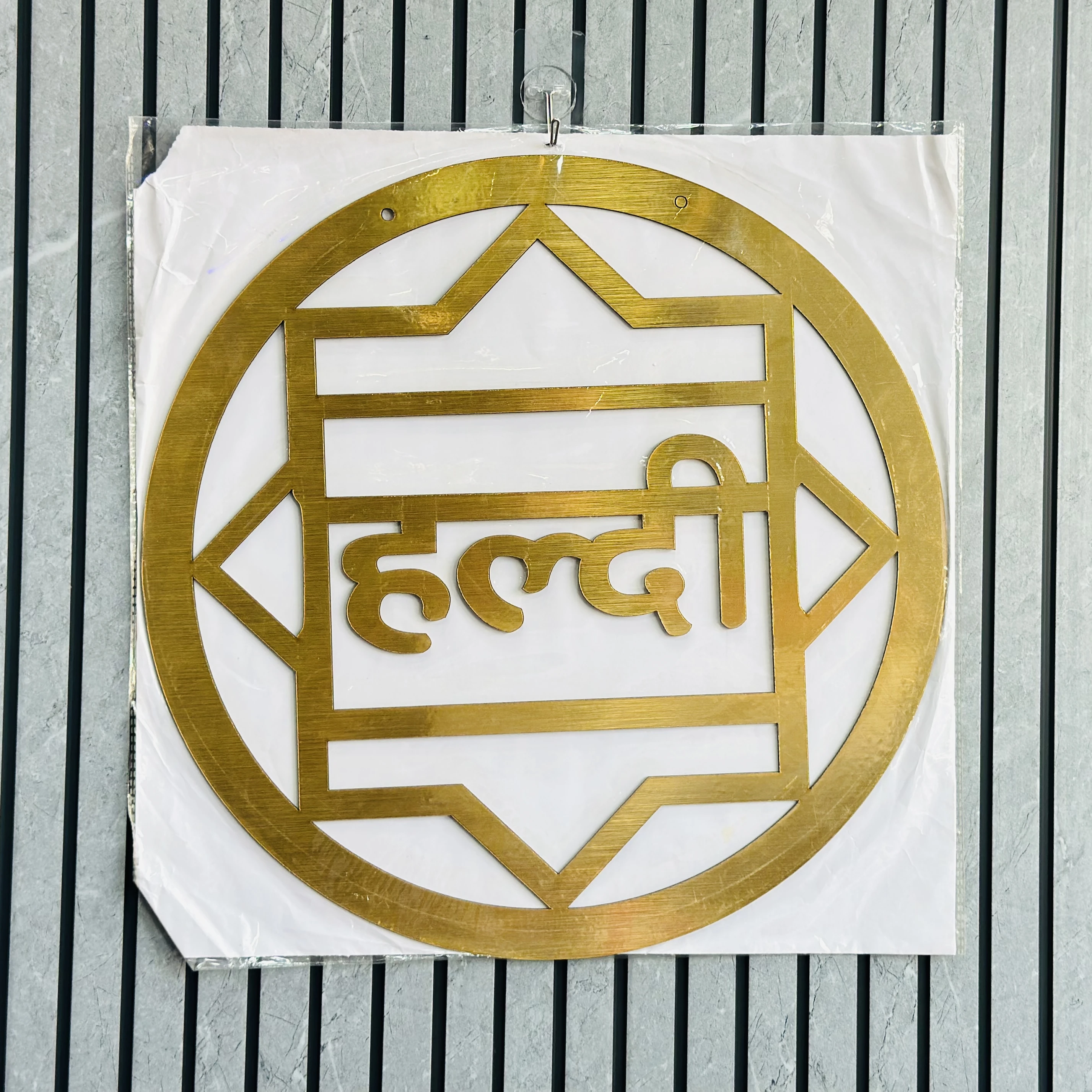 decorative brass cutout featuring the Hindi word for "turmeric" (हल्दी, haldi)