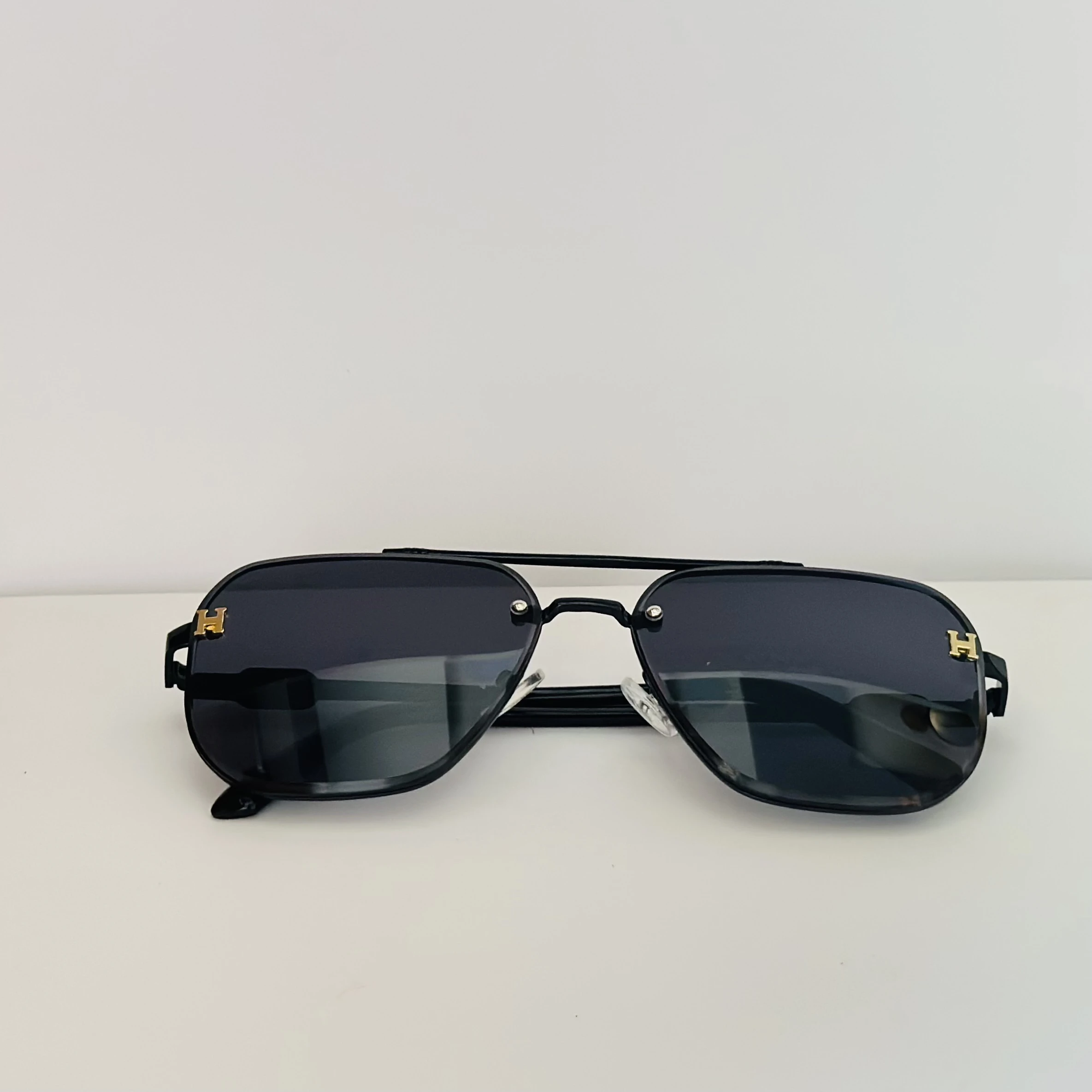 Black rimless aviator sunglasses with gold-tone "H" emblems on the temples.