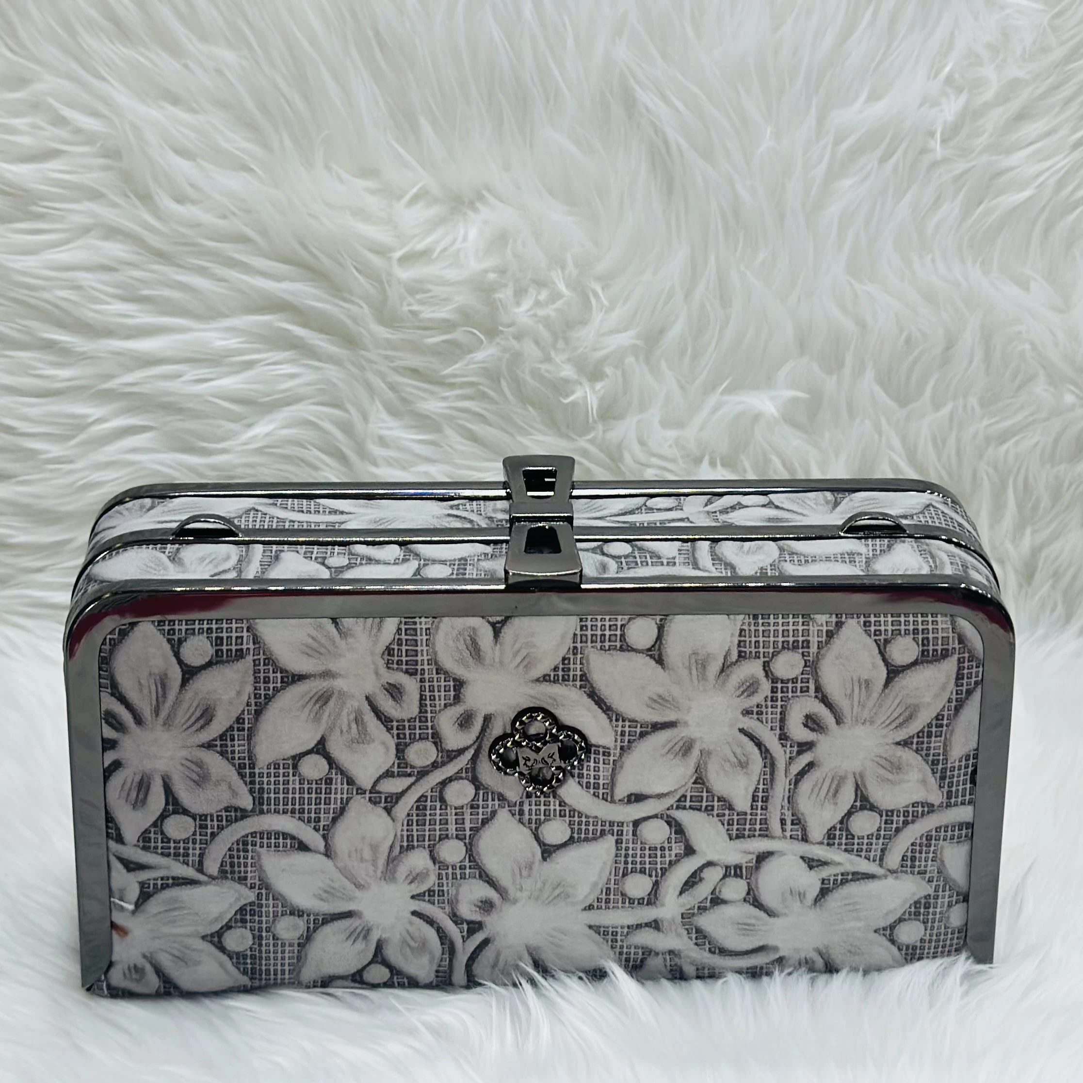 Embellished box clutch bag with a black metal frame and a floral pattern.
